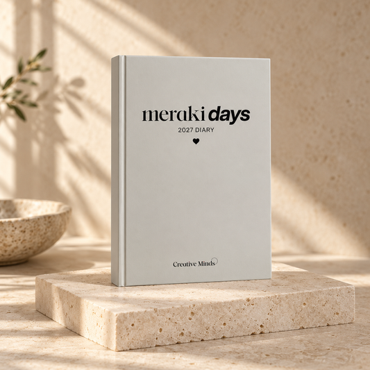 Meraki Days 2027 Daily Diary with grey cover and black lettering, styled on a warm stone plinth.